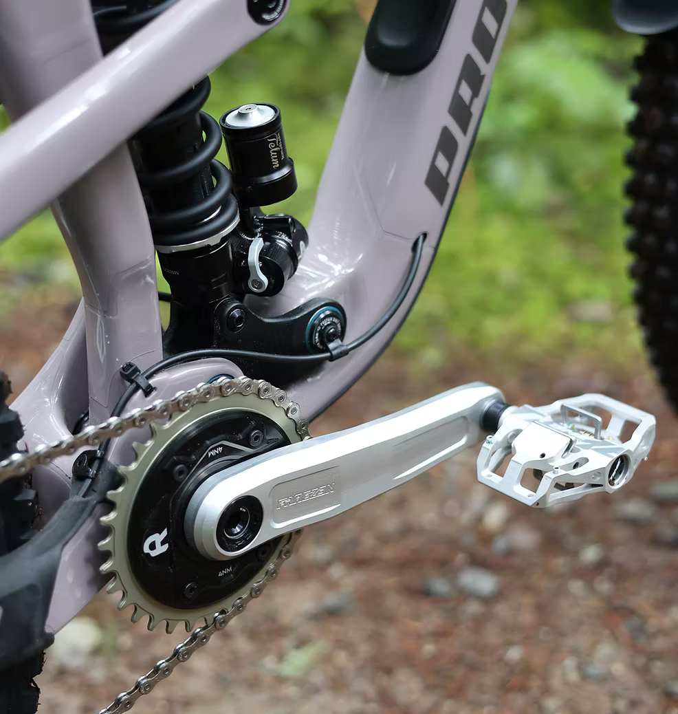 Close-up of a mountain bike drivetrain showing a Shimano Deerride crank arm, Rimpact Chain Damper, and rear suspension components on a mountain bike frame.