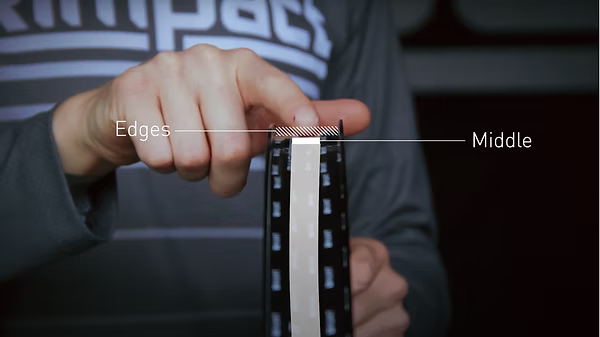 A close-up of a person's hand holding a strip of black and white film or tape, with text labels pointing to the 'Edges' and 'Middle' side.