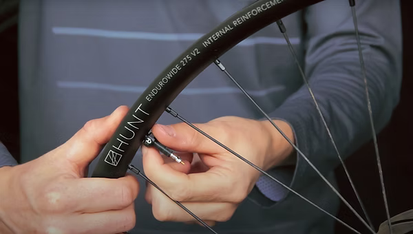 Close-up of a person's hands installing a spoke nipple onto a black Hunt Endurride 273 V2 bicycle wheel.