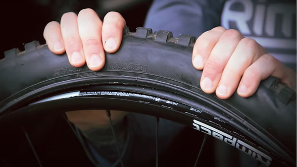Close-up of a person's hands holding a black mountain bike tire mounted on a wheel, with the brand name 'RIDE' partially visible on the rim.