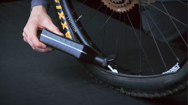A close-up of a person's hand using a black and gray bicycle tire lever to pry up a tire on a dark bicycle wheel.