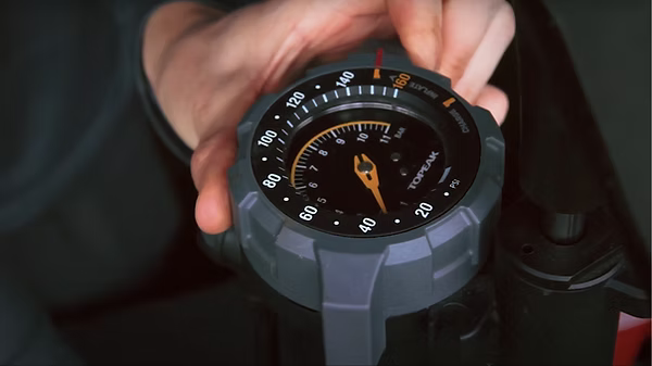 A close-up of a person's hands adjusting the dial on a rugged gray and black Topopeak bicycle pump gauge.