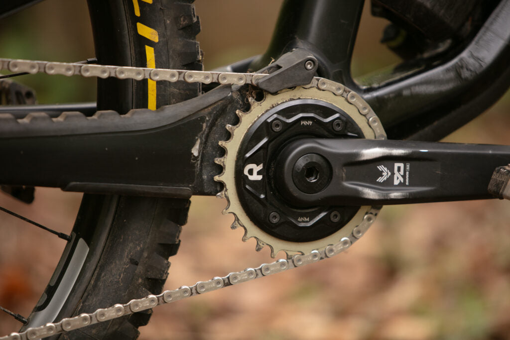 Close-up of Rimpact Chain Damper black crank arm, photographed outdoors with a blurred natural background.